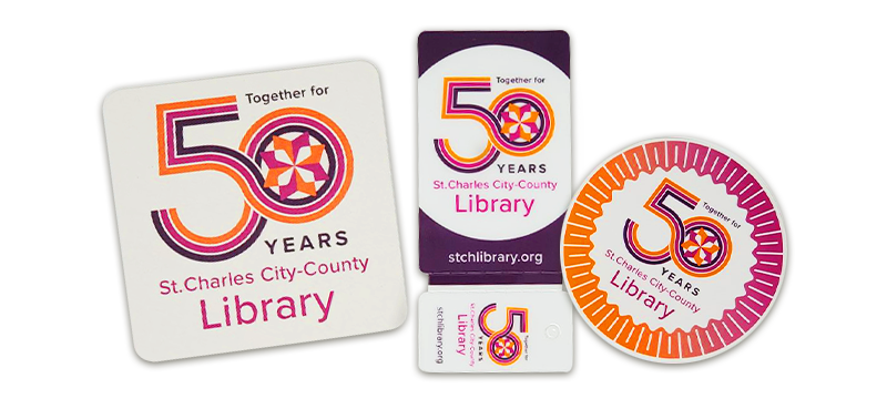 Image of 50th Anniversary giveaways; a coaster, library card, and sticker with the anniversary logo