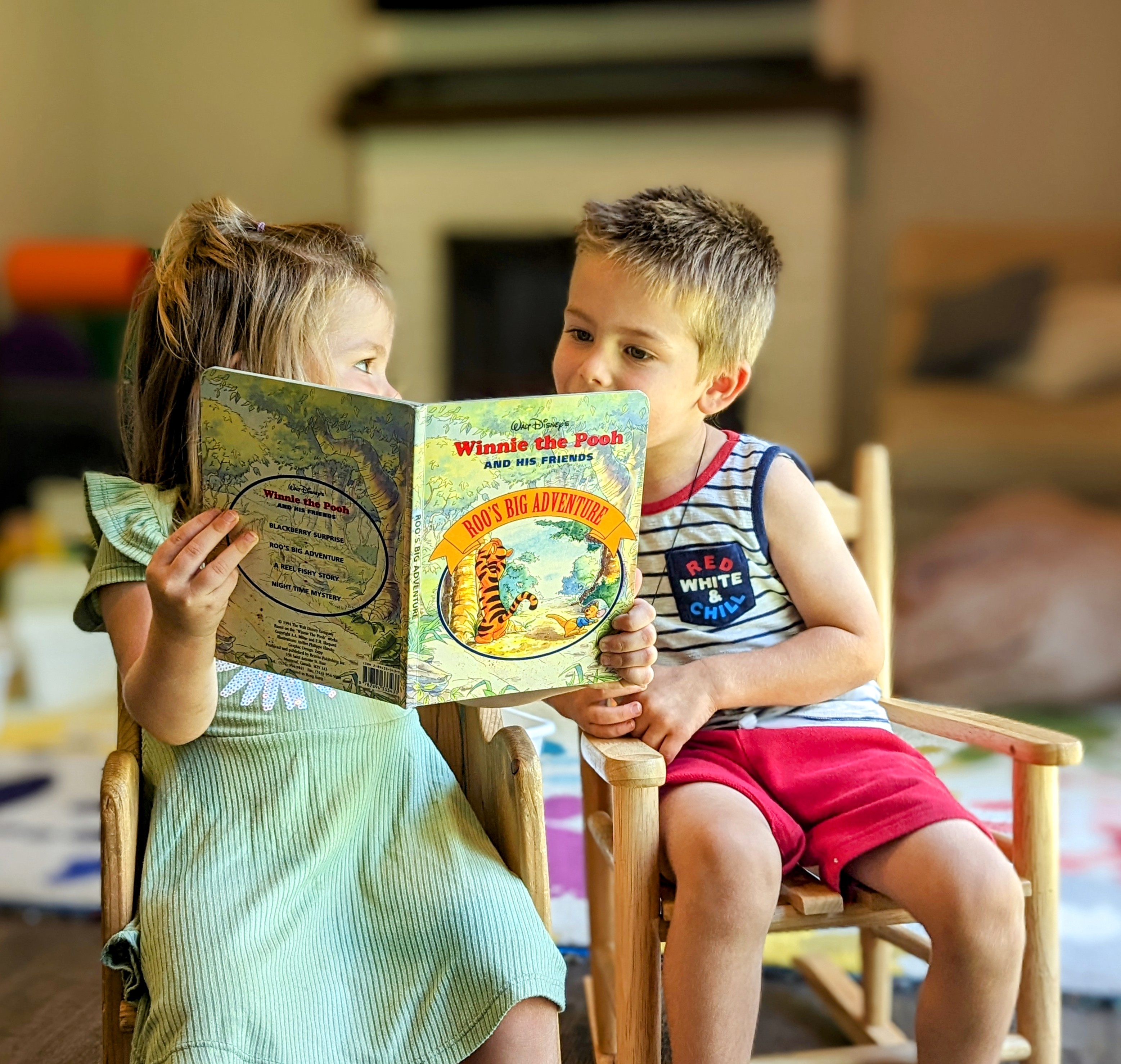 Two small children seated reading Winnie the Pooh and his Friends