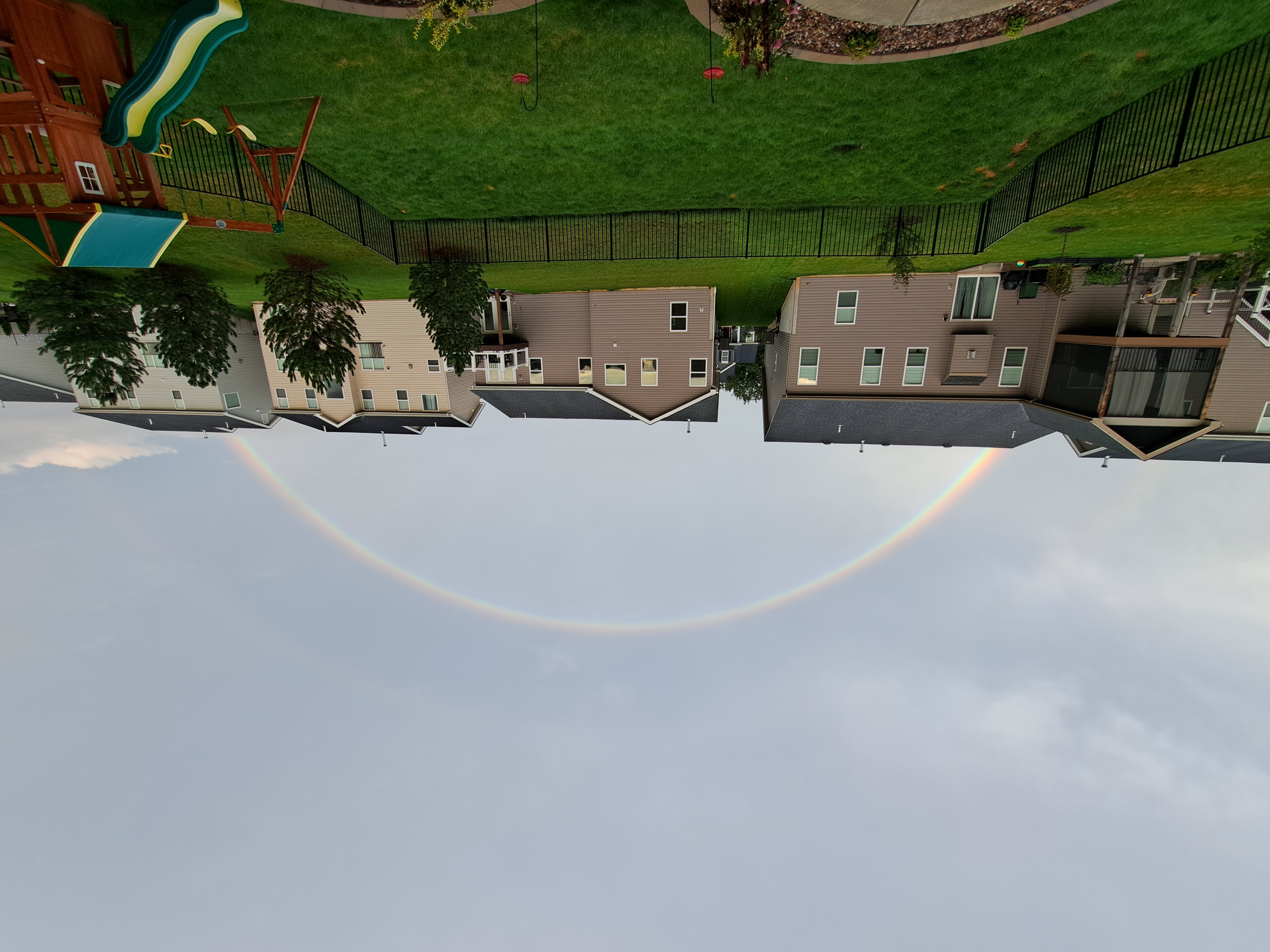 Image of a backyard with a green lawn, play place, and a large rainbow in the sky