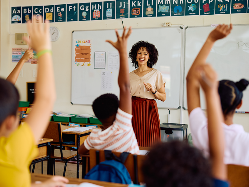 a teacher in front of her class with students raising their hands