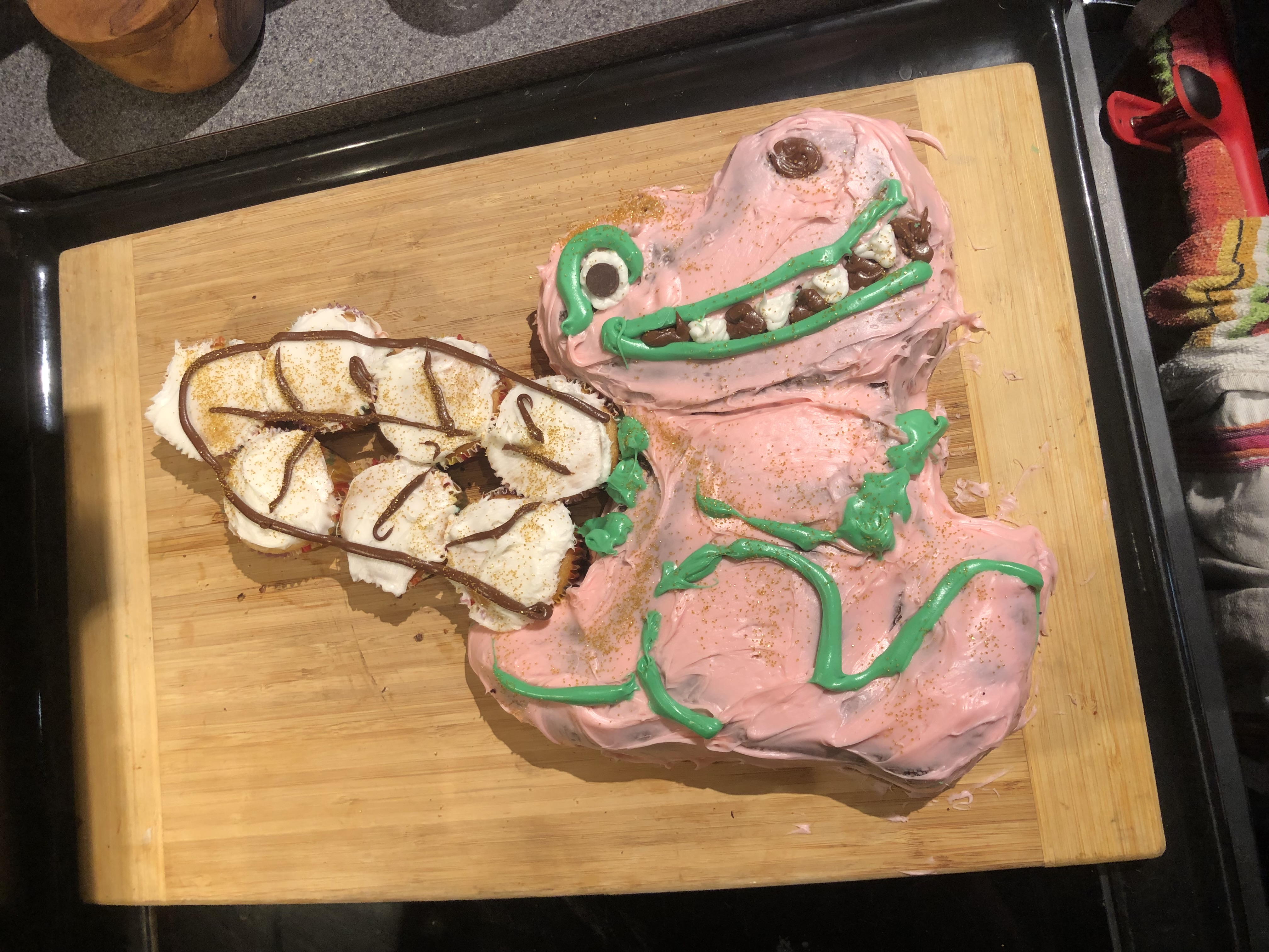 dinosaur cake with pink and green icing with wings made from cupcakes