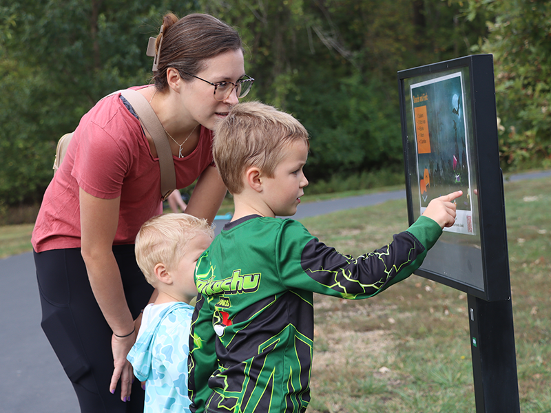 mom and two sons at the park reading the book of the Storybook Walk