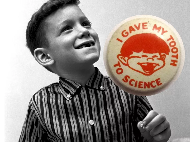 Young boy missing his front two teeth with a 1960s button reading I Gave My Tooth to Science