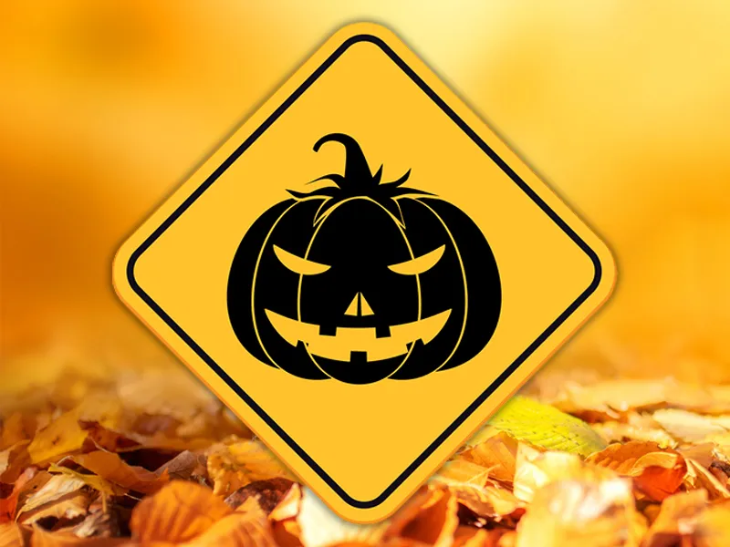 Fall background image with a yellow road sign that has a black jack-o-lantern sits in the middle.