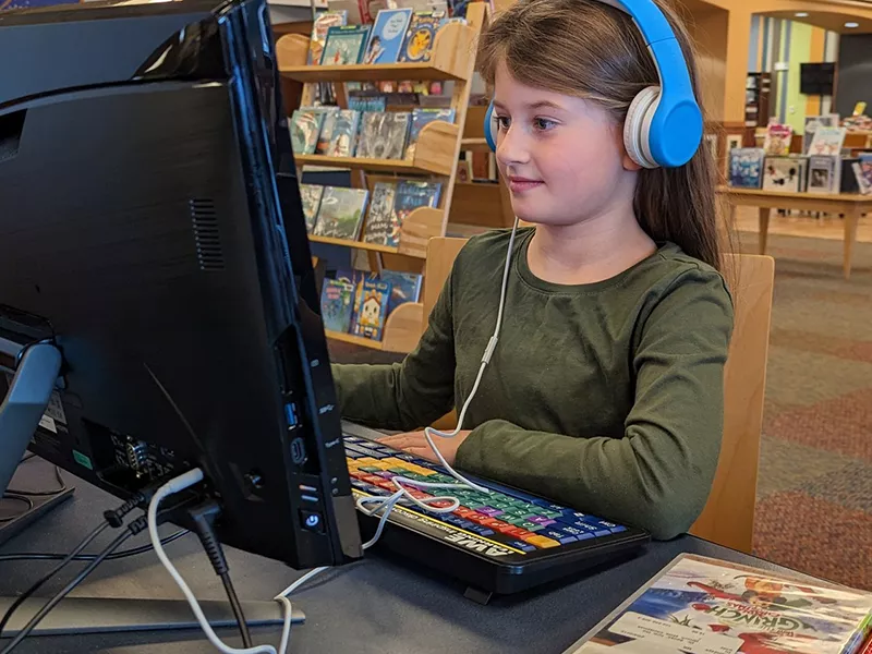 colored photo of child sitting at a modern computer with blue headphones on