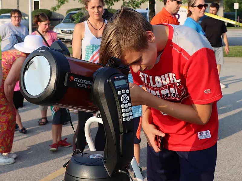 young teen looking through a library telescope